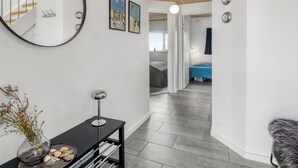 A modern interior with a round mirror, a small table with a vase and decorative items, a staircase, and a hallway leading to a bedroom with a blue bedspread.
