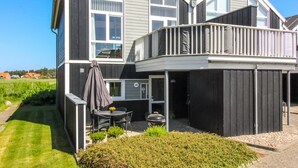 A two-story house with a balcony, a patio with outdoor furniture, and a well-maintained garden.