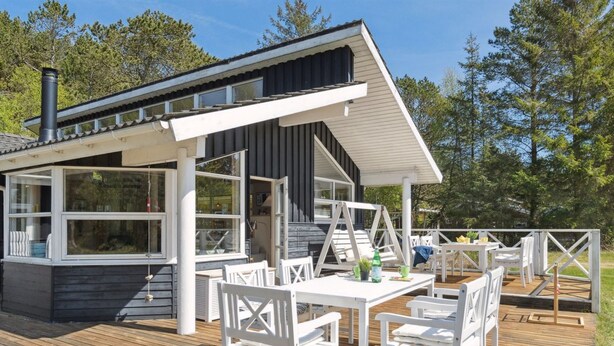 A wooden deck with white chairs and a table, a covered outdoor area with a swing, and a building with large windows and a chimney. - "Petri" - 500m from the sea by Interhome (Hals)