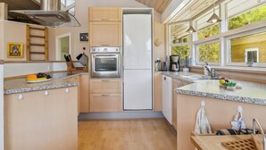 A modern kitchen with a stainless steel oven, a refrigerator, and a window with a view of greenery. - "Petri" - 500m from the sea by Interhome (Hals)
