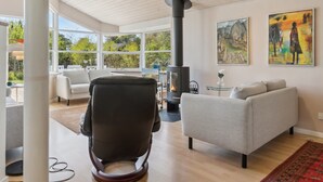 A modern living room with a large window, a black chair, a grey sofa, and a wood-burning stove. - "Petri" - 500m from the sea by Interhome (Hals)