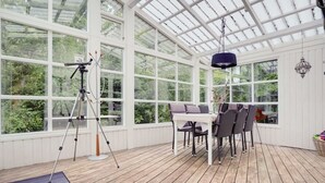 A conservatory with a wooden deck, a table with chairs, and a telescope on a tripod. - "Gunward" - 1.5km from the sea by Interhome (Sæby)