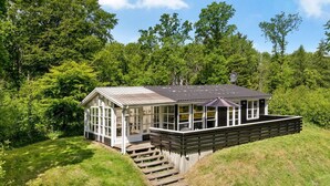 A wooden cabin with a large glass front, a deck, and a staircase leading up to it, surrounded by lush greenery. - "Gunward" - 1.5km from the sea by Interhome (Sæby)