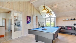 Ein geräumiger Raum mit Poolbillard, Holzwänden, einem großen Fenster und einer gemütlichen Sitzecke.