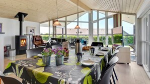 Ein modernes Wohnzimmer mit einem großen Esstisch, einem Kamin und Blick ins Freie.