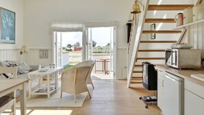 A spacious kitchen with a wooden staircase, a dining area with wicker chairs, and a view of the outdoors.