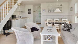 A spacious living area with a staircase, white furniture, and a kitchen area visible in the background.
