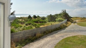 A coastal pathway leading to a grassy area with a wooden fence and a view of the sea.