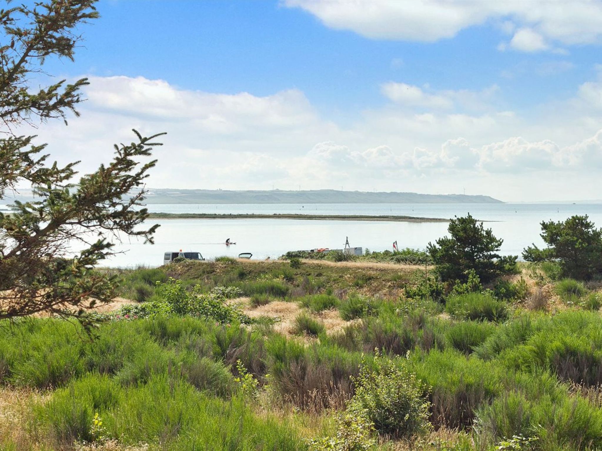 A coastal landscape with a sandy beach, dense greenery, and a clear view of the sea.