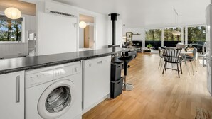 Een moderne keuken met een ingebouwde wasmachine, een eethoek met een groot raam, en een bar met uitzicht op de omgeving.