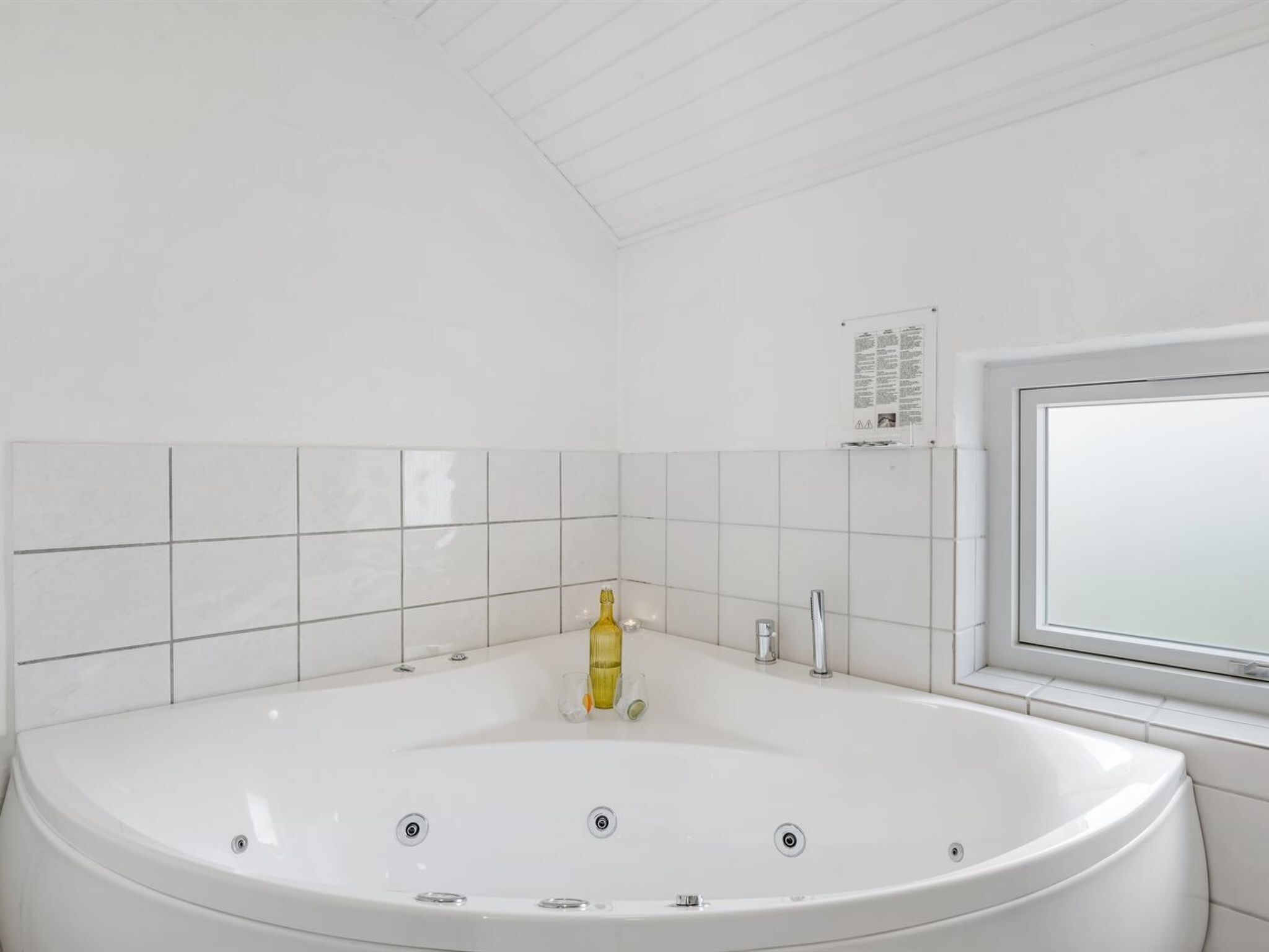 A modern bathroom with a large white bathtub, a window, and a tiled wall.