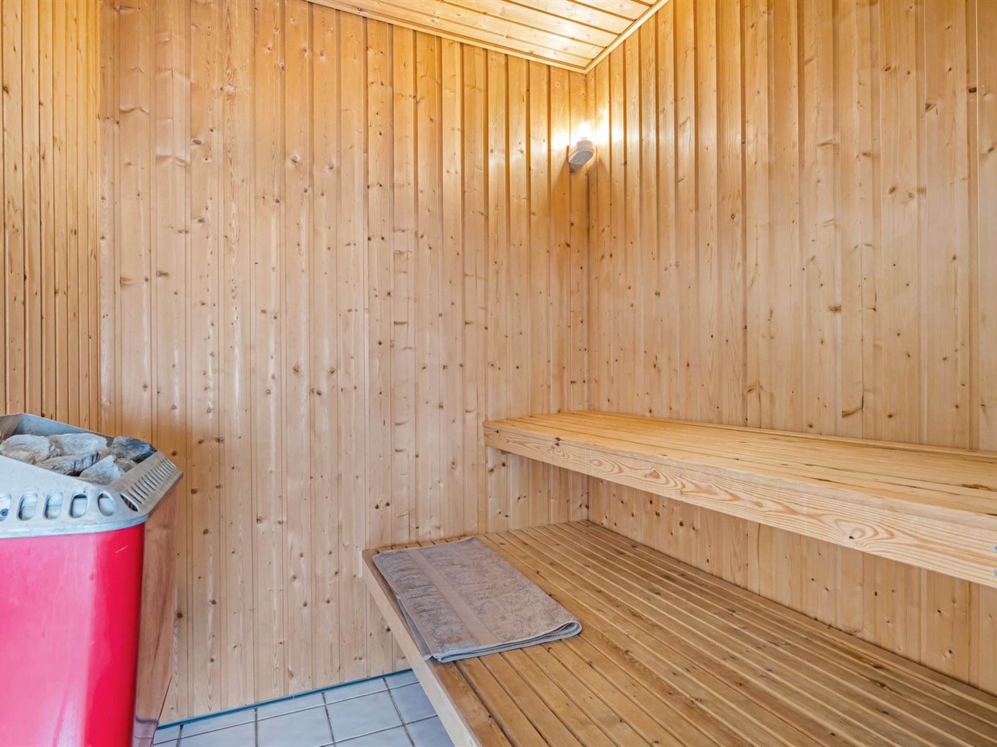 A sauna room with wooden walls, a bench, and a red container.