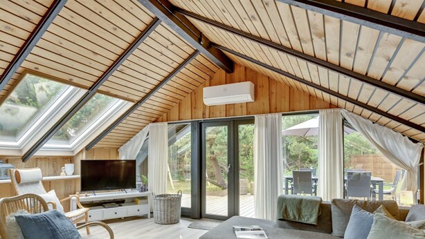 A cozy, well-lit room with a high ceiling, wooden beams, and large windows. There is a comfortable seating area with a sofa and chairs, a flat-screen TV, and a small table with candles. - "Sidse" - 400m from the sea by Interhome (Ringkøbing)