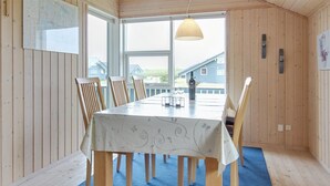 Zona pranzo con tavolo apparecchiato per sei persone, sedie in legno, tappeto blu e ampie finestre con vista sulle case circostanti.