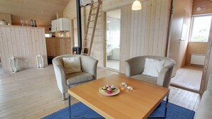 Un accogliente interno di una baita con un tavolo da pranzo in legno, due poltrone, angolo cottura con fornello e una scala.