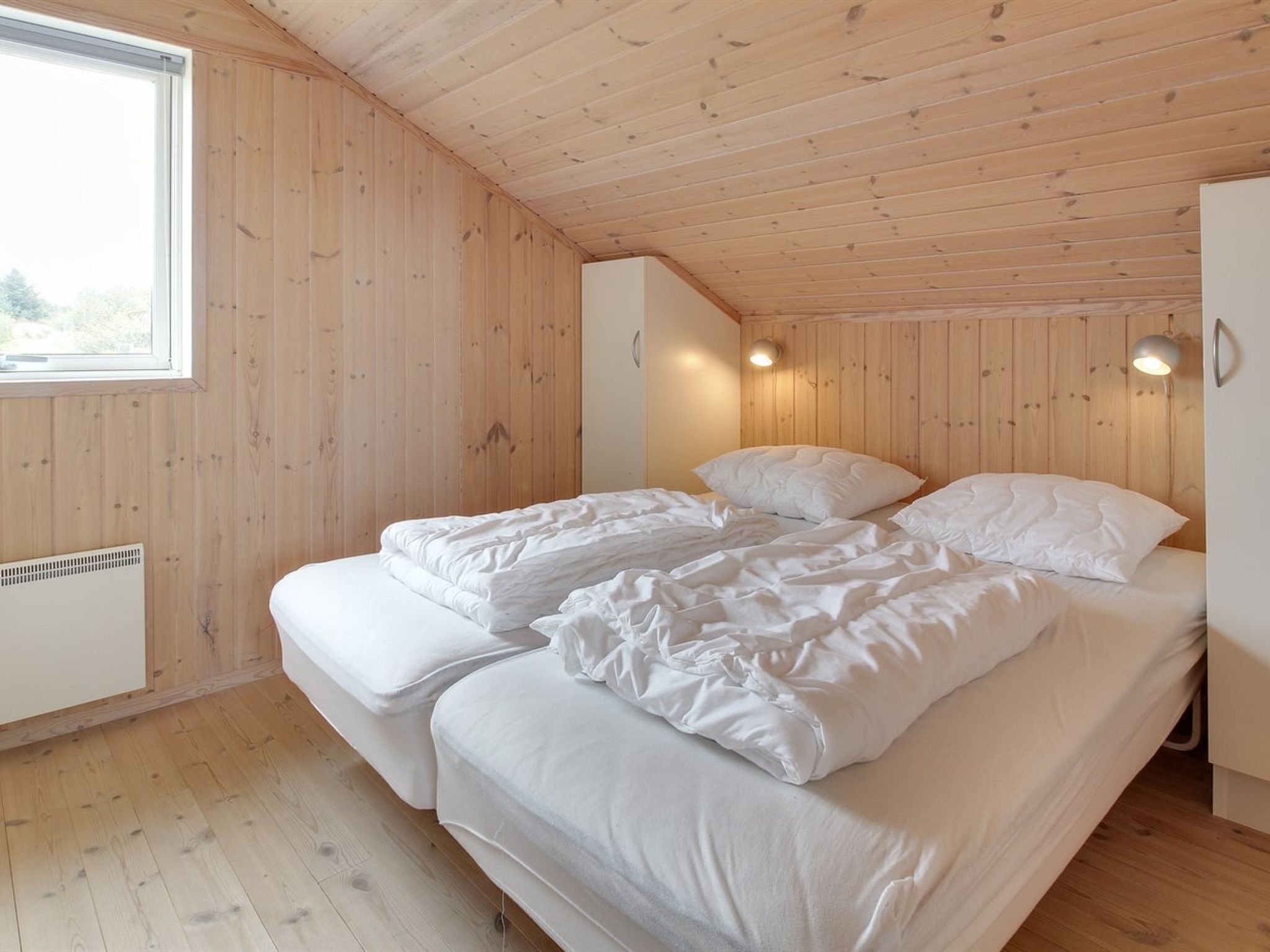 Een slaapkamer met een houten plafond en wanden, een bed met wit beddengoed, een raam en een wandlamp.