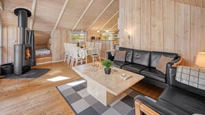 Interior acollidor d'una cabana amb zona de menjador, saló amb sofà i estufa de llenya.