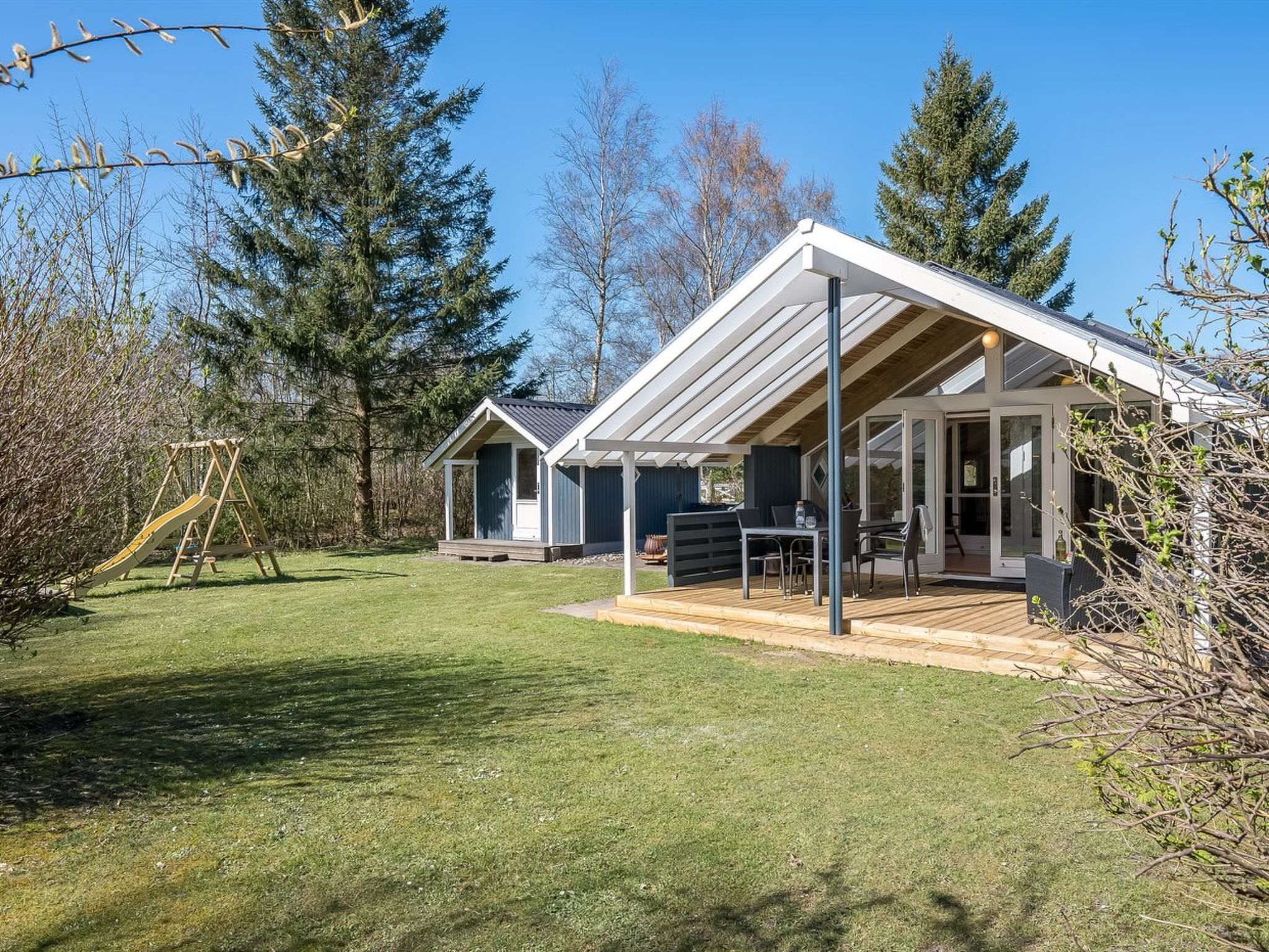 Ein modernes Haus mit überdachter Terrasse, Holzschaukel und Rasenfläche.