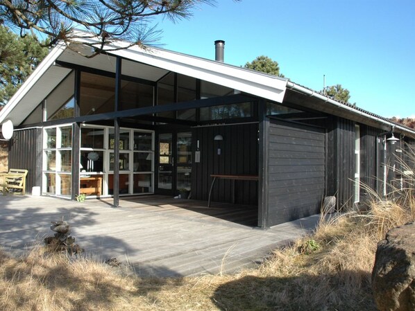 Een modern gebouw met grote ramen, een houten terras en een schoorsteen.