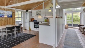 A modern kitchen with white cabinetry, a dining area with a black and white checkered table, and a large window providing a view of greenery outside. - "Alin" - 600m from the sea by Interhome (Oksbøl)