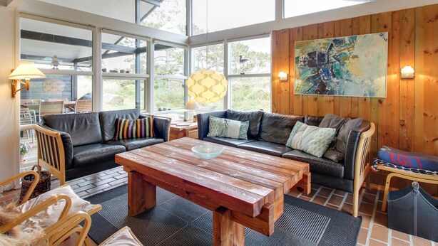 A spacious living area with a wooden ceiling, large windows, a black leather sofa, a wooden coffee table, and a wall-mounted abstract painting. - "Alin" - 600m from the sea by Interhome (Oksbøl)