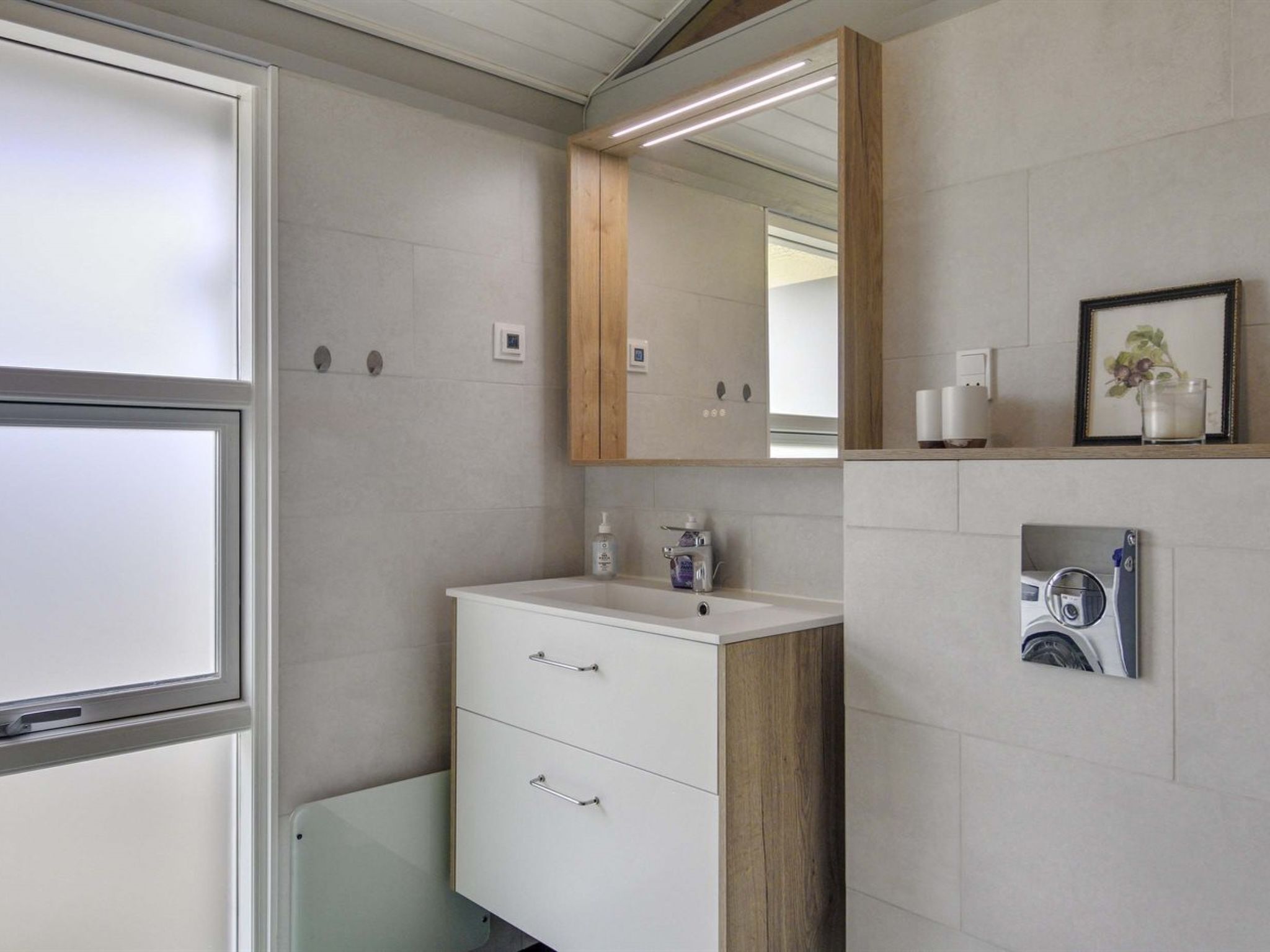 Une salle de bain moderne avec un meuble-lavabo blanc, un meuble en bois et un miroir au-dessus. Il y a deux tiroirs et un plan de travail avec un distributeur de savon.