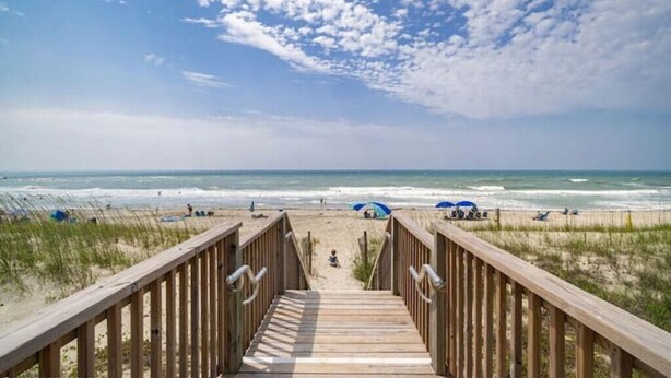 A wooden boardwalk leading to a beach with people and umbrellas.