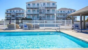A swimming pool with a white fence and lounge chairs.