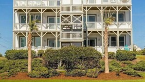 A multi-story beachfront hotel with balconies, palm trees, and dense shrubbery.