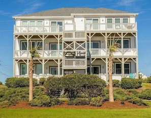 A multi-story beachfront hotel with balconies, palm trees, and dense shrubbery. - Light & Airy Oceanside Escape - Beach, Pool, & Pickleball / Tennis! (Emerald Isle)