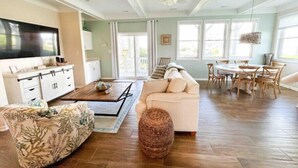 A spacious living room with a large TV, a sofa, a coffee table, and a dining area with chairs.