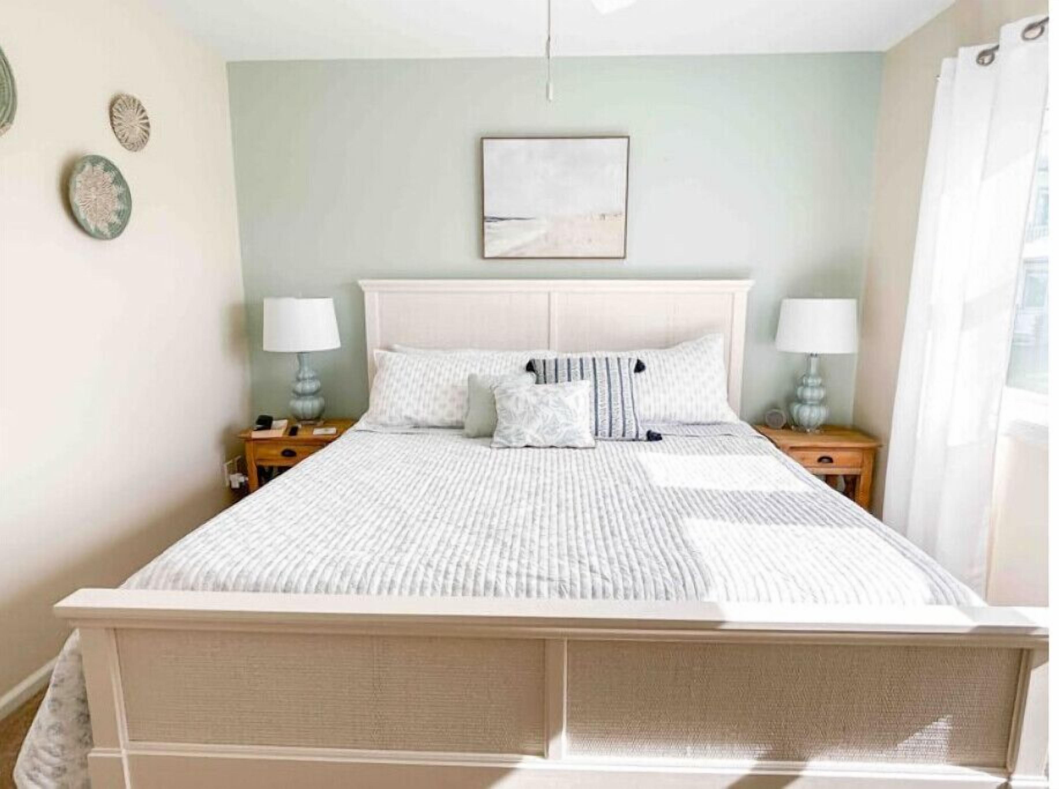 Un lit bien fait, avec une tête de lit blanche, deux tables de chevet avec des lampes et un tableau encadré au mur.