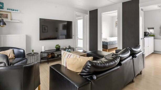 Una sala moderna con un sofá de cuero negro, un televisor y una mesita auxiliar.