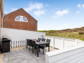 A patio with a table and chairs, a barbecue grill, and a white fence.