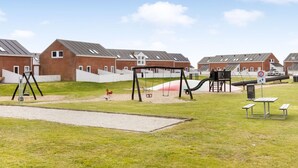 Un parque infantil con columpios y toboganes, una mesa de picnic y una señal de límite de velocidad.