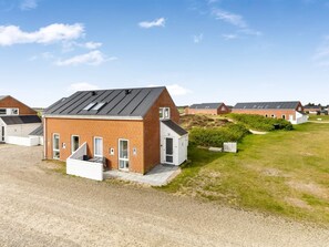 A row of modern, single-story brick houses with flat roofs and large windows, arranged in a tidy, grassy area.