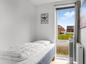 A bedroom with a bed, a radiator, and a window with a view of buildings.