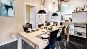 A modern kitchen with wooden cabinets, a dining area with a wooden table and chairs, and pendant lighting.