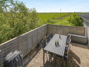 Eine Terrassengruppe mit Tisch und Stühlen, umgeben von einem Holzzaun, mit Blick auf ein grünes Feld.