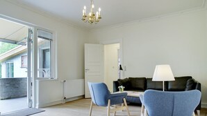 Uma sala de estar moderna com um sofá de couro preto, duas poltronas azuis, uma mesa pequena e um abajur.