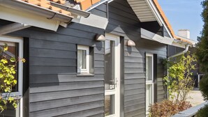 Une maison moderne avec un revêtement extérieur gris, un toit en tuiles et un petit porche doté d’un banc.