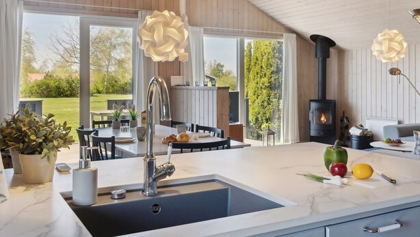 Une cuisine moderne dotée d’un grand îlot central, d’une cuisinière intégrée et de luminaires suspendus.