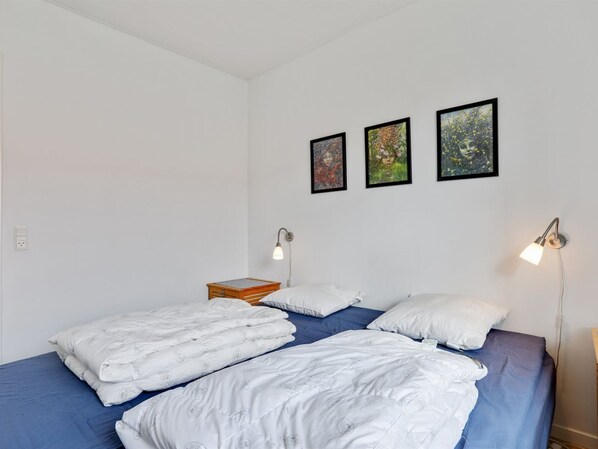 Quarto com duas camas, uma mesa de cabeceira e três quadros na parede.
