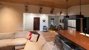 Cozinha moderna com ilha central, sala de jantar com cadeiras e sala de estar com sofá.