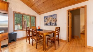 Un'area pranzo con un tavolo e sedie in legno, un quadro appeso al muro e una finestra vista alberi.