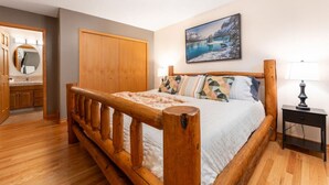 Una camera da letto con un letto in legno, un comodino, un quadro raffigurante un paesaggio innevato e un'armadio in legno.