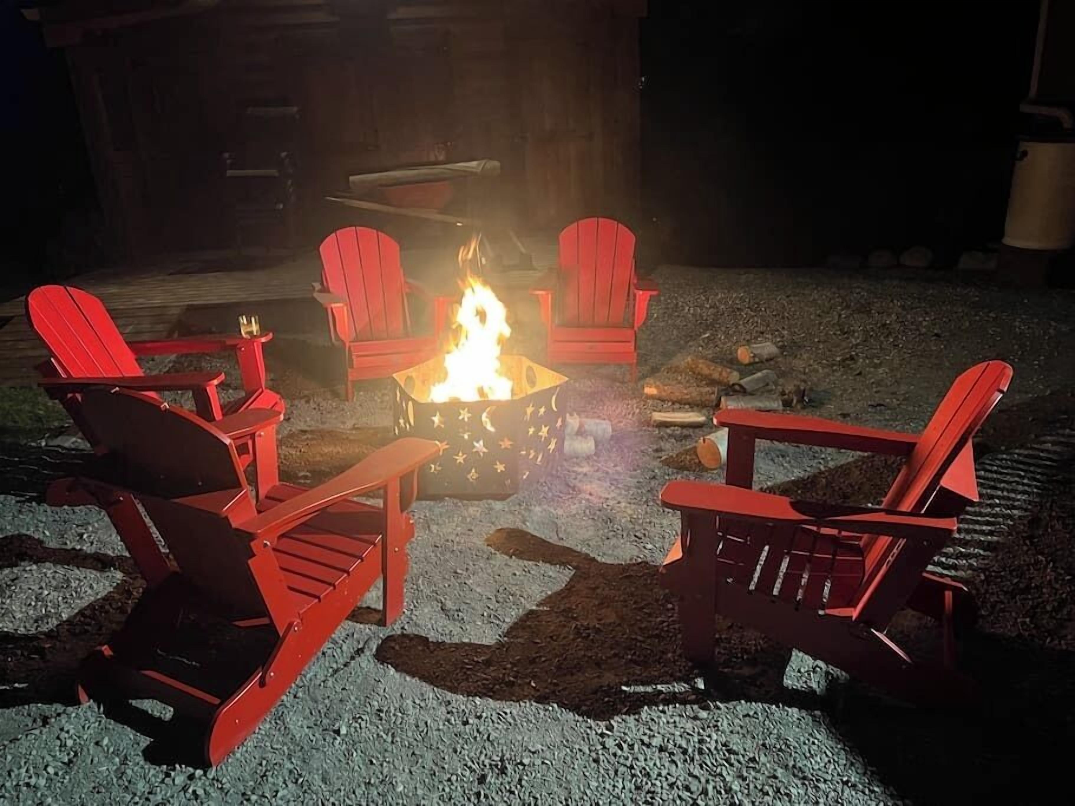 A fire pit with four red Adirondack chairs arranged around it.