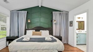 Une chambre avec un grand lit, deux tables de chevet, un banc et une vue sur la salle de bain.