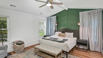 A bedroom with a bed, bedside tables, a bench, a ceiling fan, and a window with curtains.