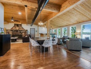 Un amplio salón con chimenea de piedra, techo de madera y grandes ventanales con vistas al exterior.